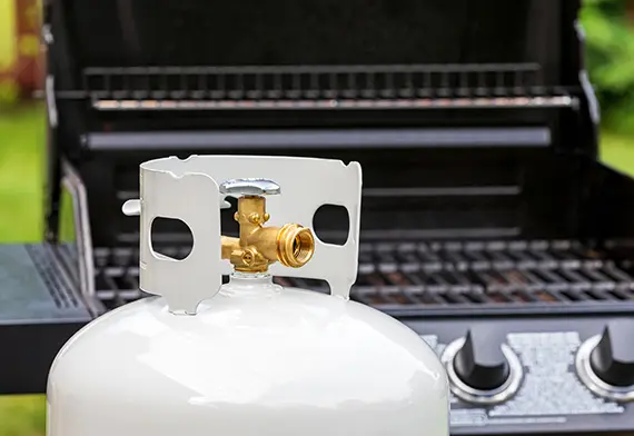 Propane cannister sitting in front of BBQ.