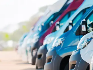 A fleet of white commercial cargo vans parked closely together in a lot, ideal for delivery services, contractors, utility work, and business fleets. The vans feature rear safety mesh windows and some include ladder racks, showcasing reliable work vehicles ready for transportation, logistics, and service industries.